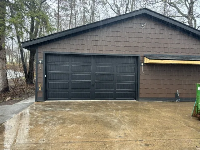 Black garage door on a brown shingle-sided detached garage