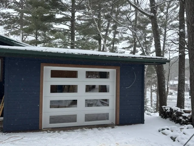 Modern frosted-glass aluminum garage door on a blue lake cabin in winter